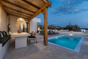 A poolside area with a covered seating area, lounge chairs, and a pool. - Golden Sand Villas (Naxos)