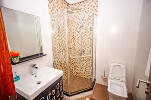 Bathroom features a glass-enclosed shower, sink, and toilet, with a small potted plant adding a touch of greenery.