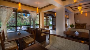 A restaurant with wooden tables and chairs, large windows with curtains, and hanging pendant lights. - Hotel 100 Petals - Gangtok 12 mins from MG Marg (Gangtok)