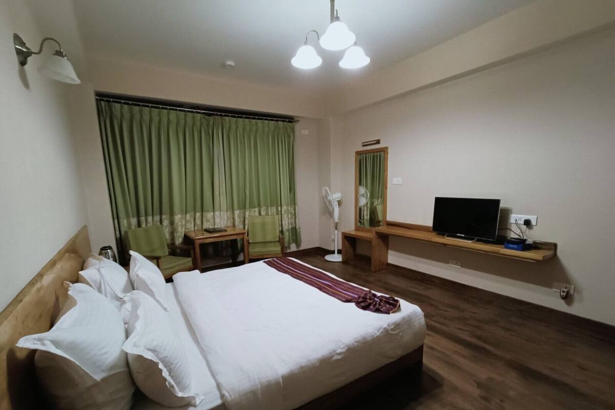 A hotel room with a large bed, a desk, a TV, and a window with curtains.