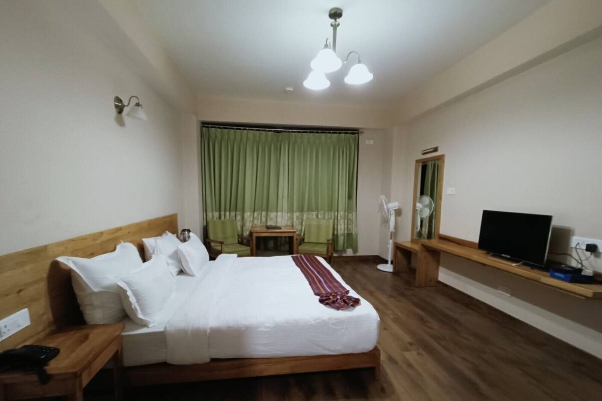 A hotel room with a wooden bed, a desk, a chair, a television, and a mirror.