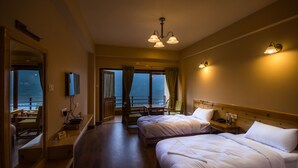 A hotel room with two beds, a balcony with a view, and a dining area with a table and chairs. - Hotel 100 Petals - Gangtok 12 mins from MG Marg (Gangtok)