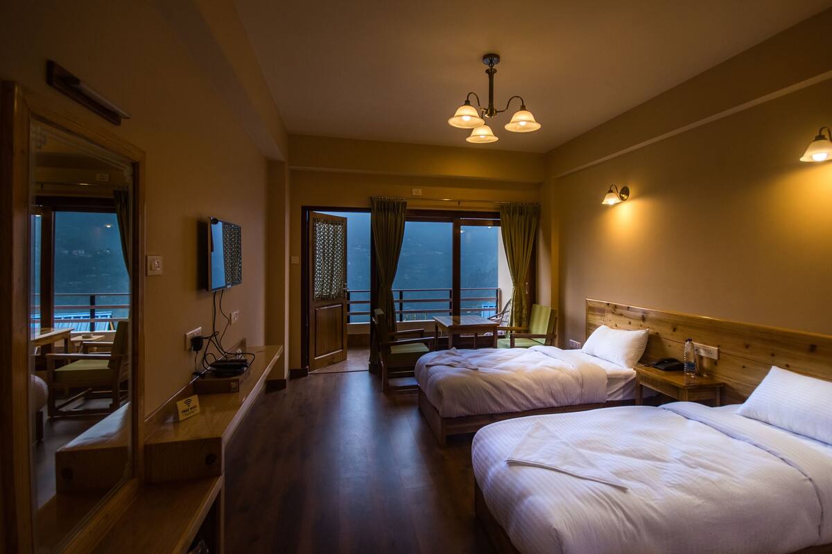 A hotel room with two beds, a balcony with a view, and a dining area with a table and chairs.
