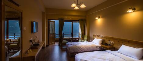 A hotel room with two beds, a balcony with a view, and a dining area with a table and chairs.