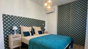 Un dormitorio con cama, mesitas de noche, lámpara, manta color turquesa y cabecera estampada.