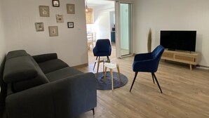 Una sala de estar moderna con un sofá, sillas, un televisor y un ventanal corredero que da a un comedor.