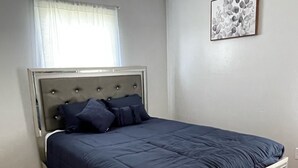 Une chambre à coucher avec un lit, un plancher en bois, une fenêtre avec des rideaux et un tableau encadré au mur.