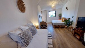A cozy living room with a sofa, a bed, a television, and a window with natural light. - Simple beach house, 6 minute walk to the beach, mountain views (Setúbal)