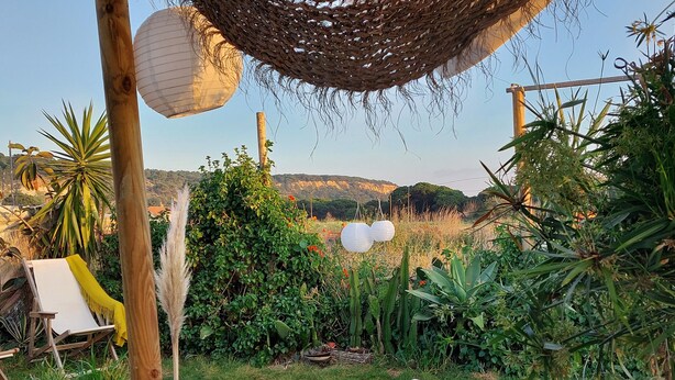 A garden with a wooden pergola, white cushions, and a yellow chair. - Simple beach house, 6 minute walk to the beach, mountain views (Setúbal)