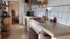 A kitchen with white tiles, wooden shelves, a sink, and a stove. - Simple beach house, 6 minute walk to the beach, mountain views (Setúbal)