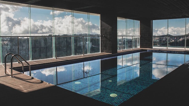 An indoor swimming pool with clear glass walls and a view of the sky and clouds. - The Plaza Lodge Baguio (Baguio)