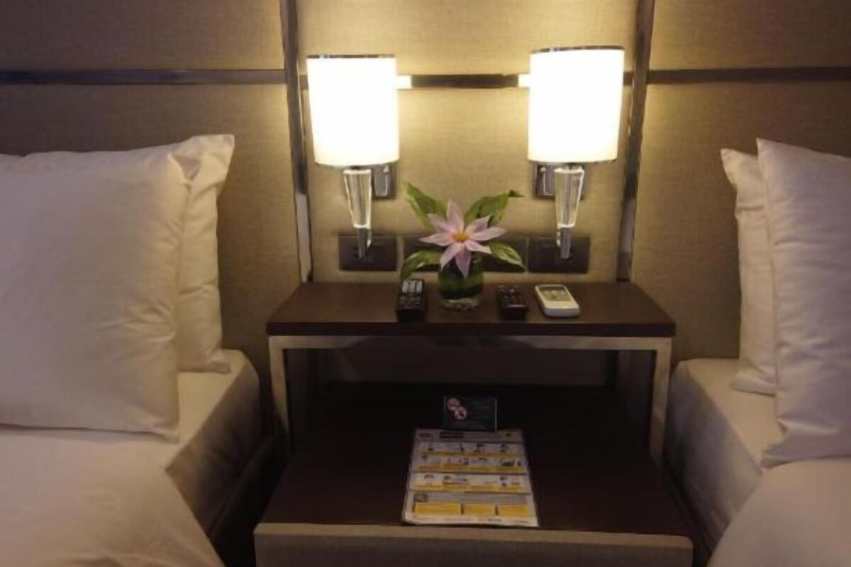 Ein Hotelzimmer mit einem Bett, zwei Nachttischen, einer Lampe, einer Blume und einer Zeitschrift.