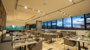 A modern restaurant with multiple dining tables and chairs, large windows with a view of the sunset, and a clean, contemporary interior design. - The Plaza Lodge Baguio (Baguio)