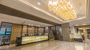 A modern hotel lobby with a reception desk, a Christmas tree, and a dessert display. - The Plaza Lodge Baguio (Baguio)