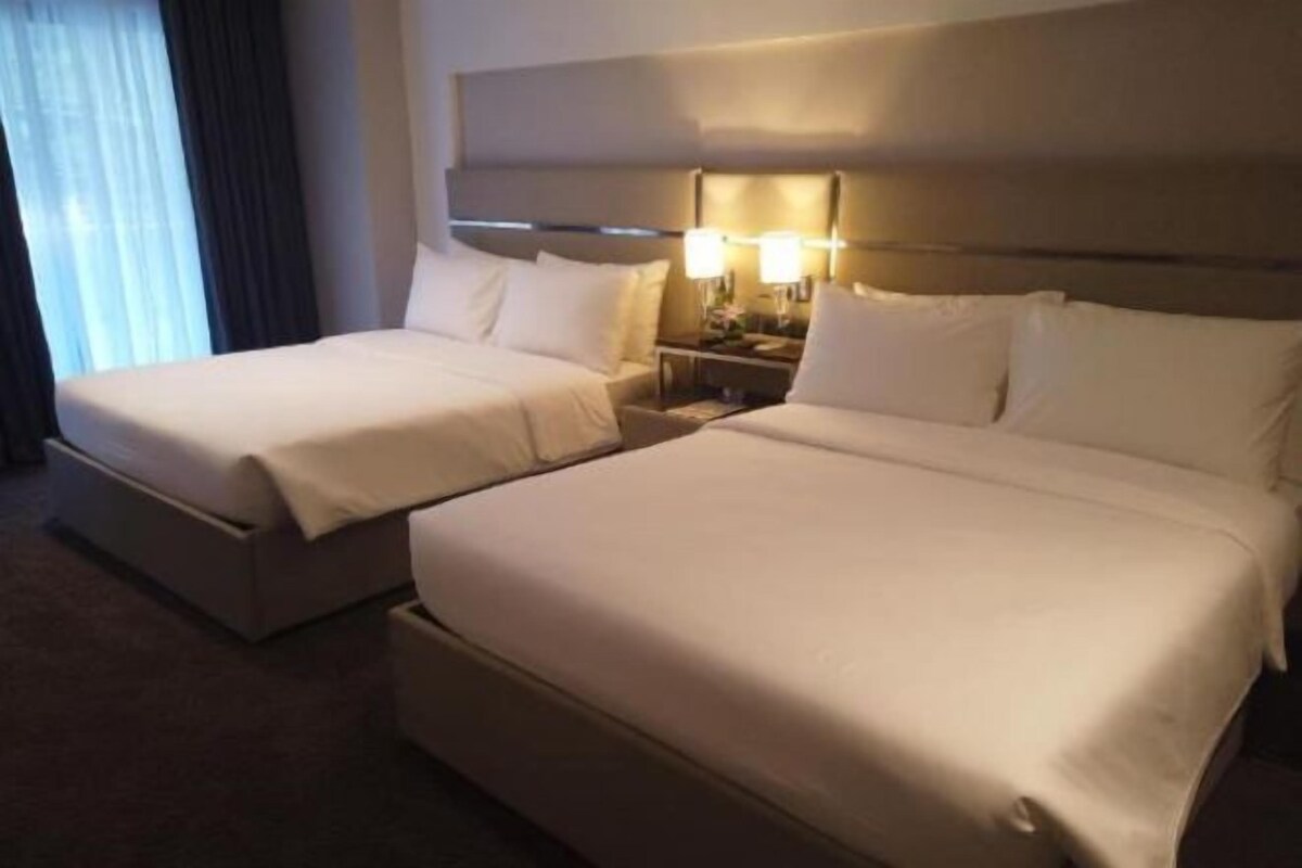Ein Hotelzimmer mit zwei Betten, einem Kopfteil, Nachttischlampen und einem Fenster mit Vorhängen.