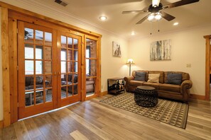 A spacious living room with a wooden floor, a leather sofa, a coffee table, and a ceiling fan.