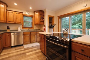 A modern kitchen with wooden cabinets, stainless steel appliances, and a large window offering a view of the outdoors.