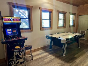A pool table, arcade games, and windows with blinds.