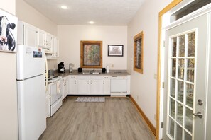 A kitchen with white cabinets, a refrigerator, a stove, and a window with blinds.