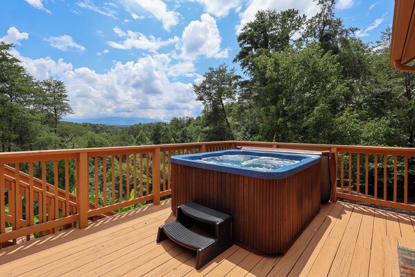 A hot tub on a wooden deck with a view of a forested landscape.
