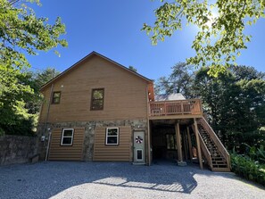 Une cabane en bois à deux étages, dotée d’un balcon, de fondations en pierre et d’une allée gravillonnée.