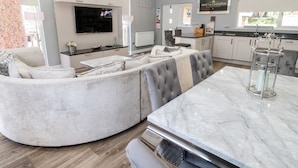 A modern living room with a curved sofa, a marble dining table, and a flat-screen TV mounted on the wall. - Lodge 32 (Newcastle-upon-Tyne)