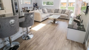 A modern living room with a sofa, chairs, and a coffee table. There is a kitchen area with cabinets and a dining table. - Lodge 32 (Newcastle-upon-Tyne)