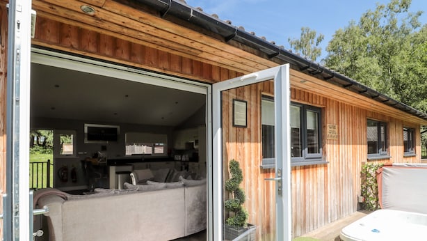 A wooden cabin with an open sliding door revealing a living area with a sofa and a dining table. - Lodge 32 (Newcastle-upon-Tyne)