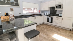 A modern kitchen with white cabinets, a granite countertop, and stainless steel appliances. There is a bar area with stools and a sign that reads "MOËT & CHANDON CHAMPAGNE". - Lodge 32 (Newcastle-upon-Tyne)