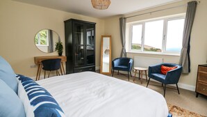 A bedroom with a large bed, a desk, a chair, a wardrobe, and a window with a view. - Ty Ni (New Quay)