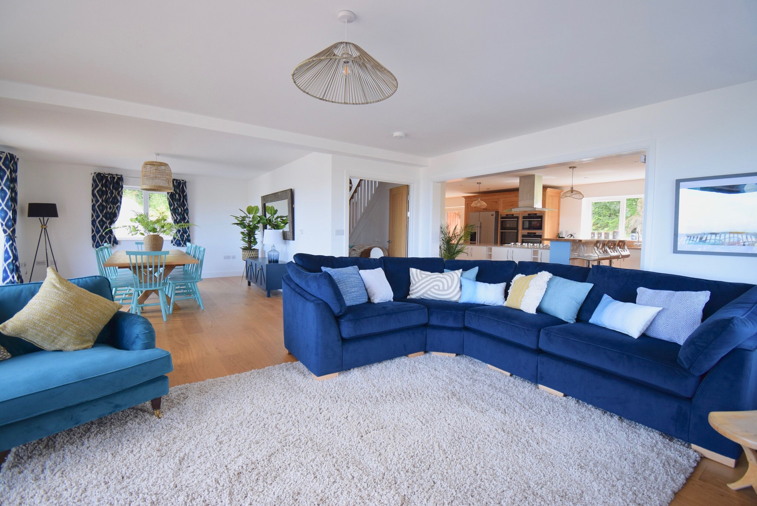 A spacious living room with a blue sectional sofa, a dining area with a table and chairs, and a kitchen in the background.