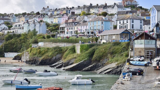 A coastal town with colorful houses, a rocky shoreline, and boats docked at the pier. - Ty Ni (New Quay)