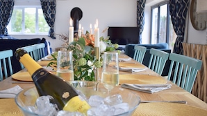 A dining table set with candles, a bottle of champagne, and glasses in a bowl of ice. - Ty Ni (New Quay)
