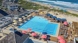 A swimming pool with sun loungers and umbrellas, a beach with people, and a view of the ocean. - Sea Salt & Sand w/ Heated Pool + Near the Beach (Corolla)