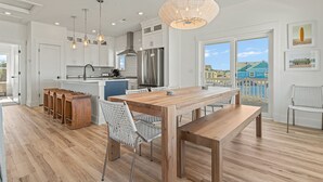 A modern kitchen with a large island, wooden flooring, and a dining area with a bench and chairs. - Sea Salt & Sand w/ Heated Pool + Near the Beach (Corolla)