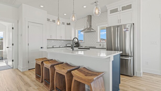 A modern kitchen with white cabinets, a stainless steel refrigerator, and a large island with bar stools. - Sea Salt & Sand w/ Heated Pool + Near the Beach (Corolla)