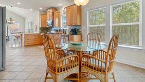 A spacious kitchen with wooden cabinets, a glass dining table, and wicker chairs. - OBX Ridgeview 4 Bedroom Home at Southridge (Nags Head)