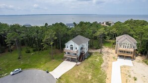 A two-story house with a front deck and a garage, surrounded by trees and a view of the sea. - OBX Ridgeview 4 Bedroom Home at Southridge (Nags Head)