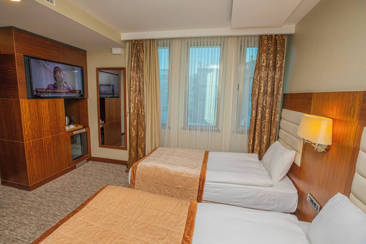 Habitación de hotel con dos camas, televisión, minibar y ventana con cortinas.