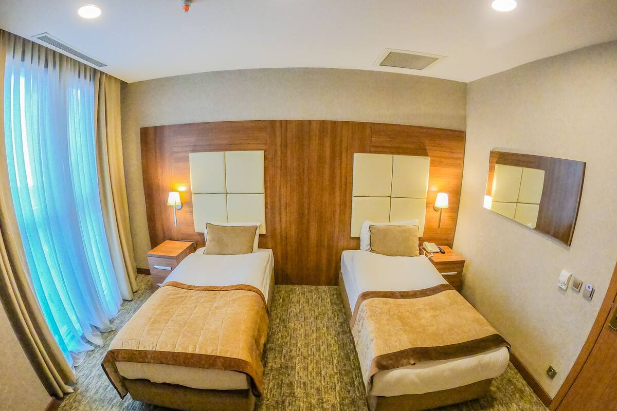 Habitación de hotel con dos camas, cabeceros de madera, lámparas de noche, un espejo grande y piso alfombrado.