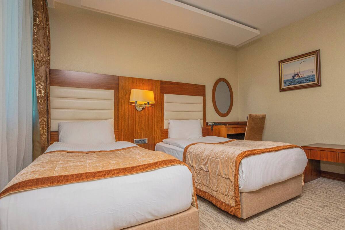 Habitación de hotel con dos camas, un escritorio, una silla, una lámpara, un espejo y un cuadro en la pared.