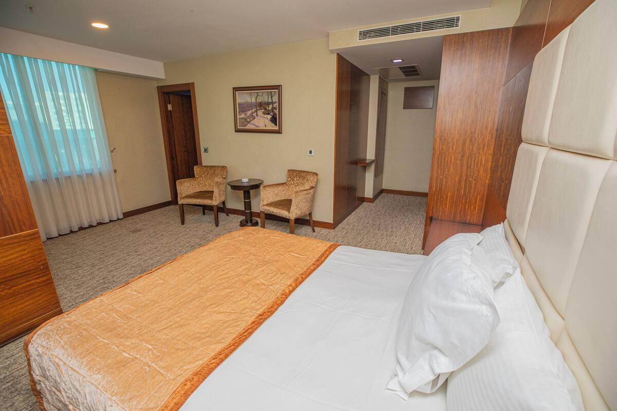 Una habitación de hotel con una cama grande, dos sillones, una mesita pequeña y un cuadro en la pared.