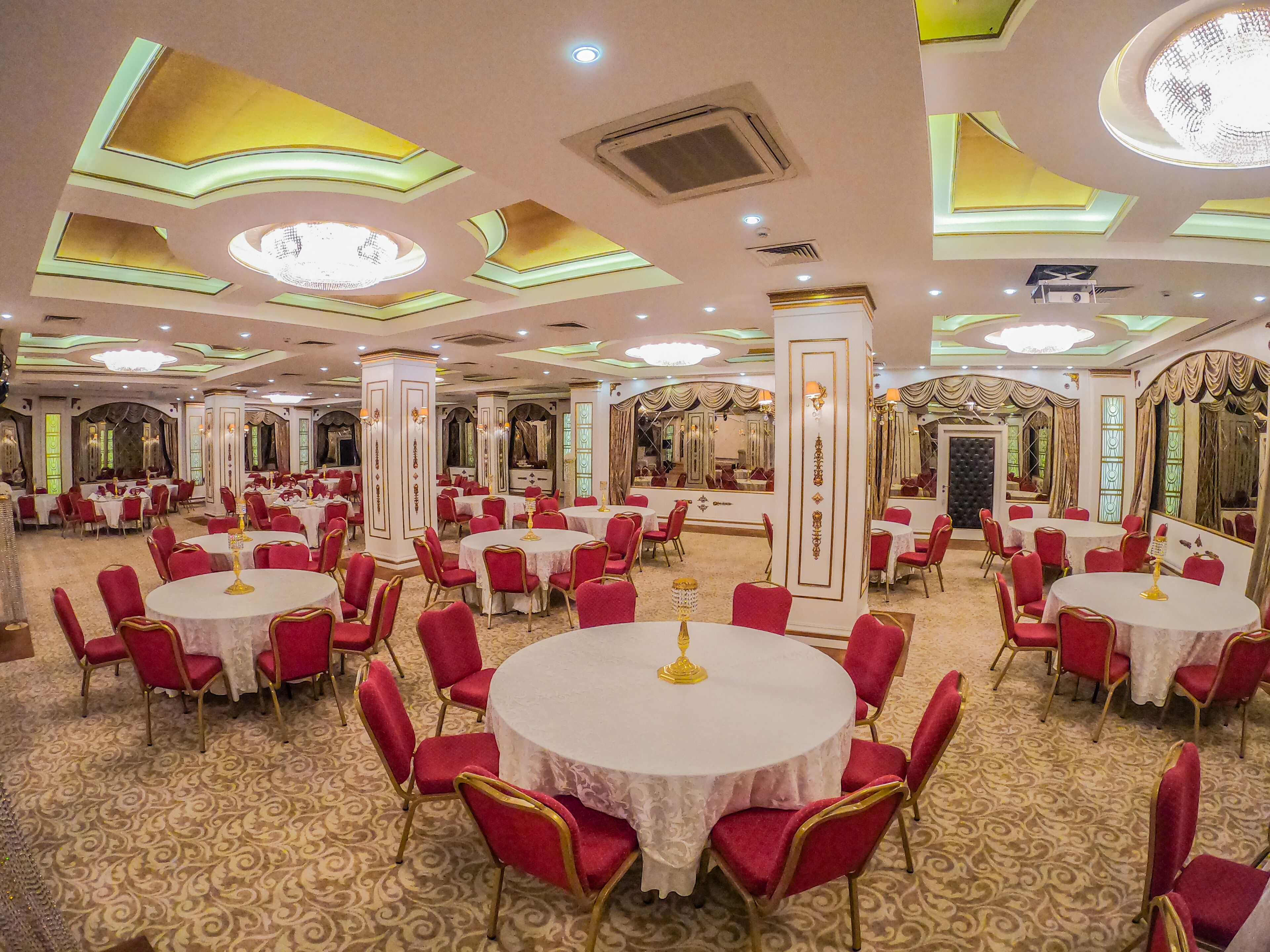 A banquet hall with round tables, red chairs, and ornate ceiling designs.
