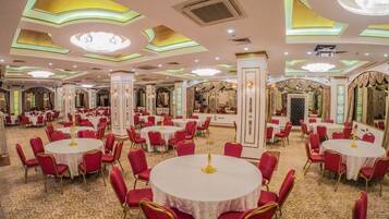 A banquet hall with round tables, red chairs, and ornate ceiling designs.