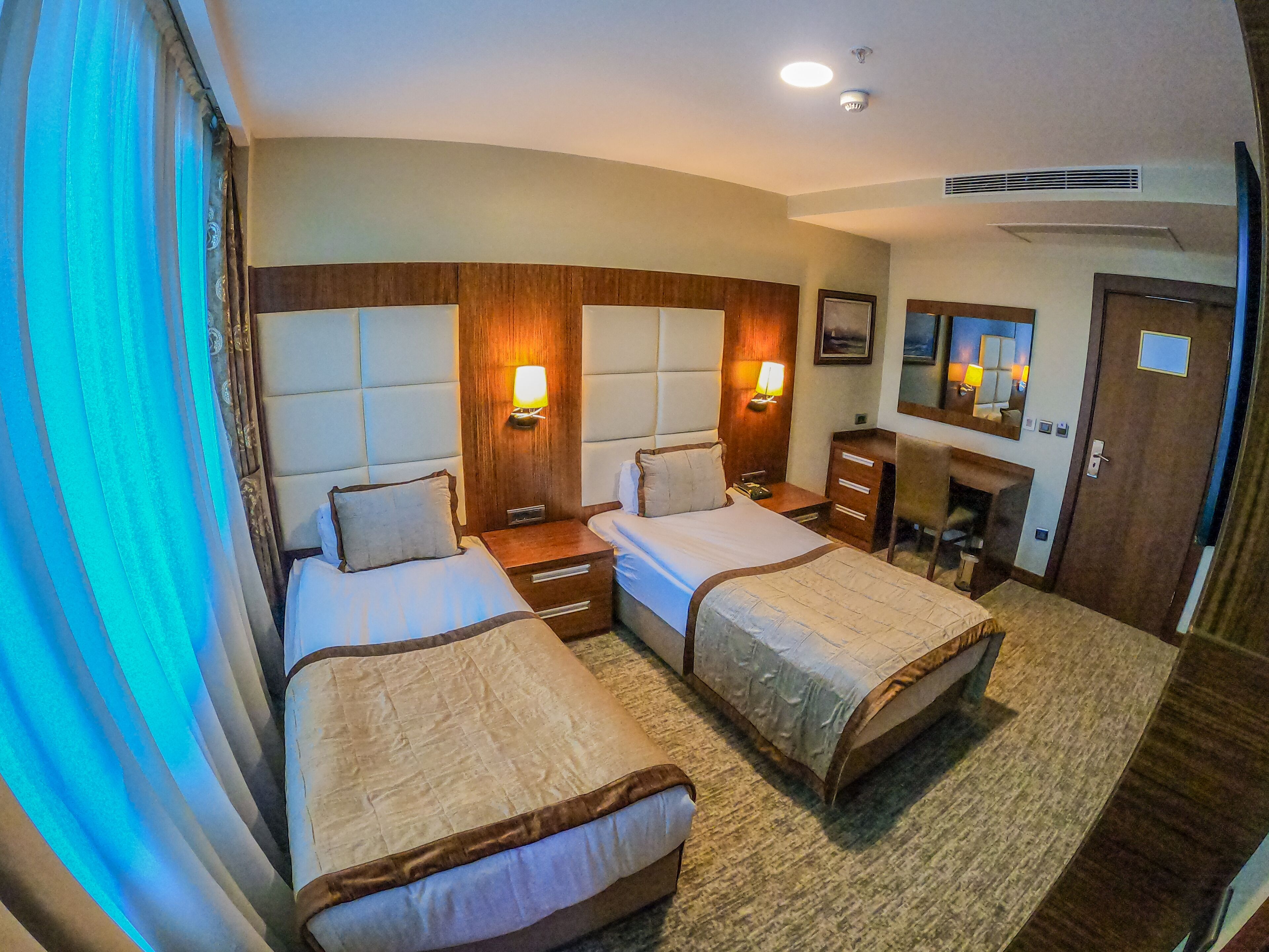 A hotel room with two beds, a desk, a chair, a dresser, and a mirror.