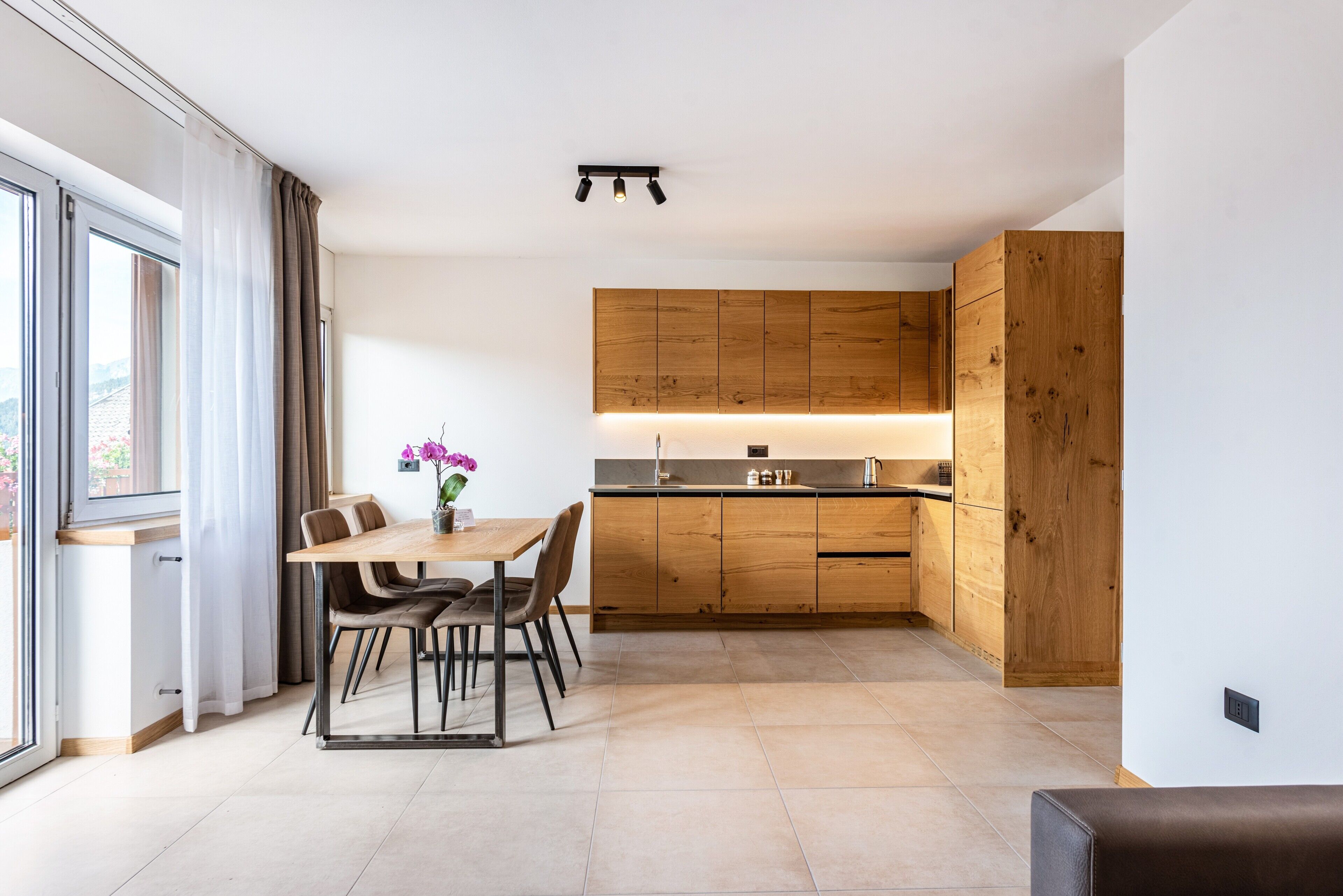 Una cocina moderna con armarios de madera, una mesa de comedor con sillas y vistas a través de un gran ventanal.