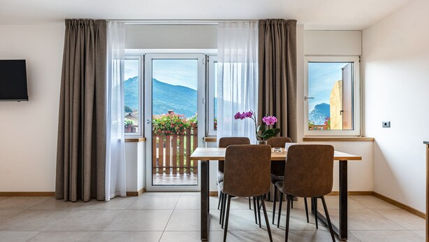 Un coin repas avec une table et des chaises, un téléviseur fixé au mur et une vue sur les montagnes par les fenêtres.