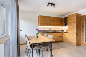 A modern kitchen with wooden cabinets, a dining table with chairs, and a small potted plant. - Apartment 'Cima Brenta' with Wi-Fi (San Lorenzo Dorsino)
