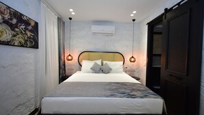 A neatly made bed with a headboard, two wall-mounted lamps, and an air conditioning unit above. - Otel Gülayvalık (Ayvalik)