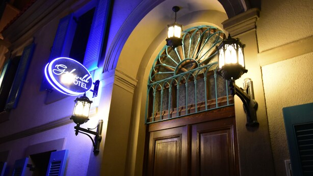 A hotel entrance with a neon sign, a wrought iron gate, and wall-mounted lanterns. - Otel Gülayvalık (Ayvalik)